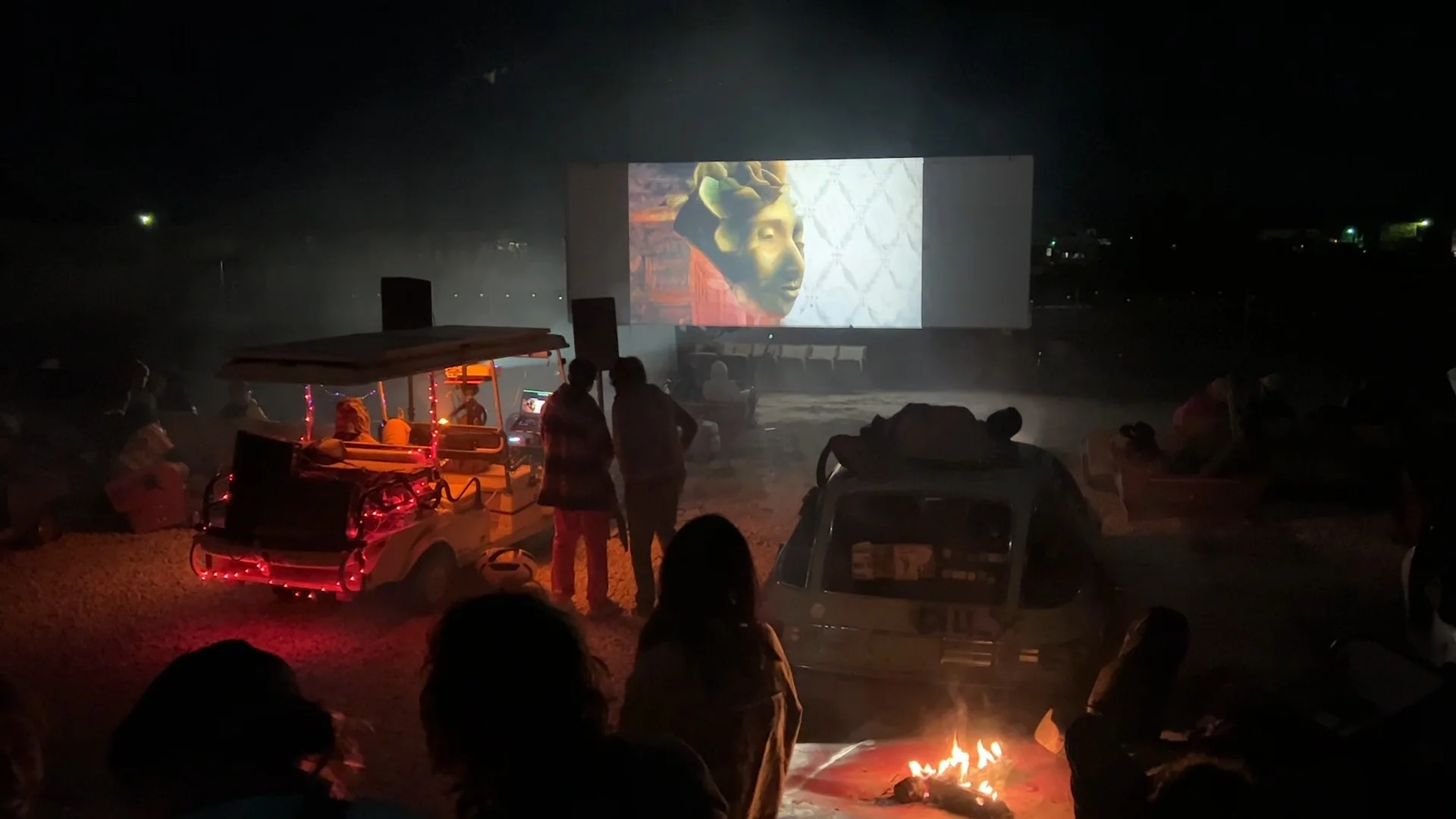 An open-air screening in the desert at Bombay Beach: the film on a drive-in screen, a fire and the town parked around it.