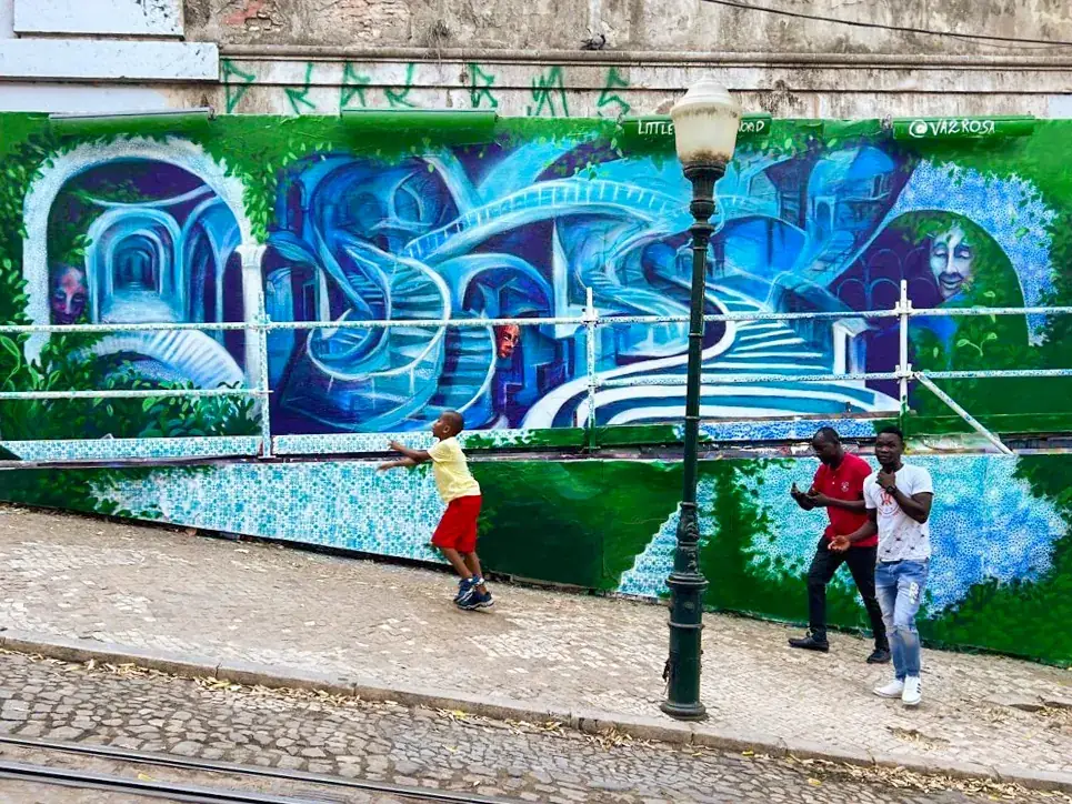 The mural on Calçada da Glória, blue staircases and arches above a green wall, a boy and two men passing in front of it.