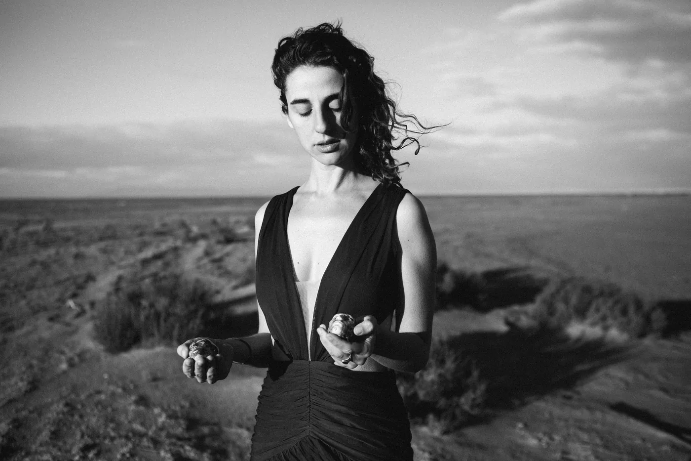 Vanessa Rosa in the desert, holding ceramic heads in both hands, in black and white.