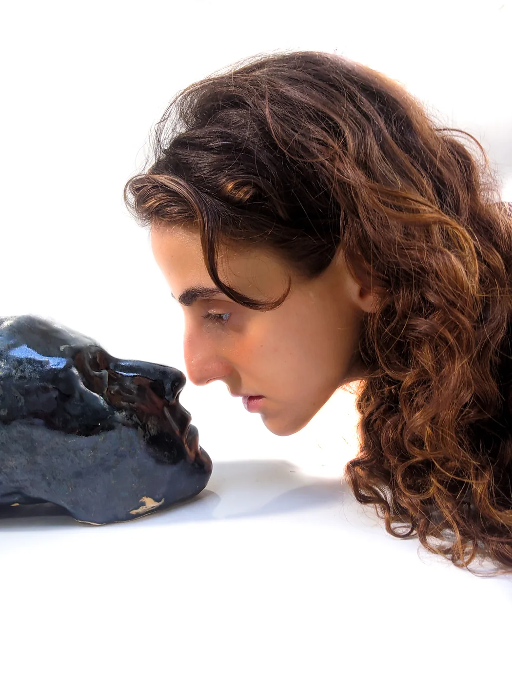 Vanessa Rosa in profile, face to face with a dark glazed ceramic head.