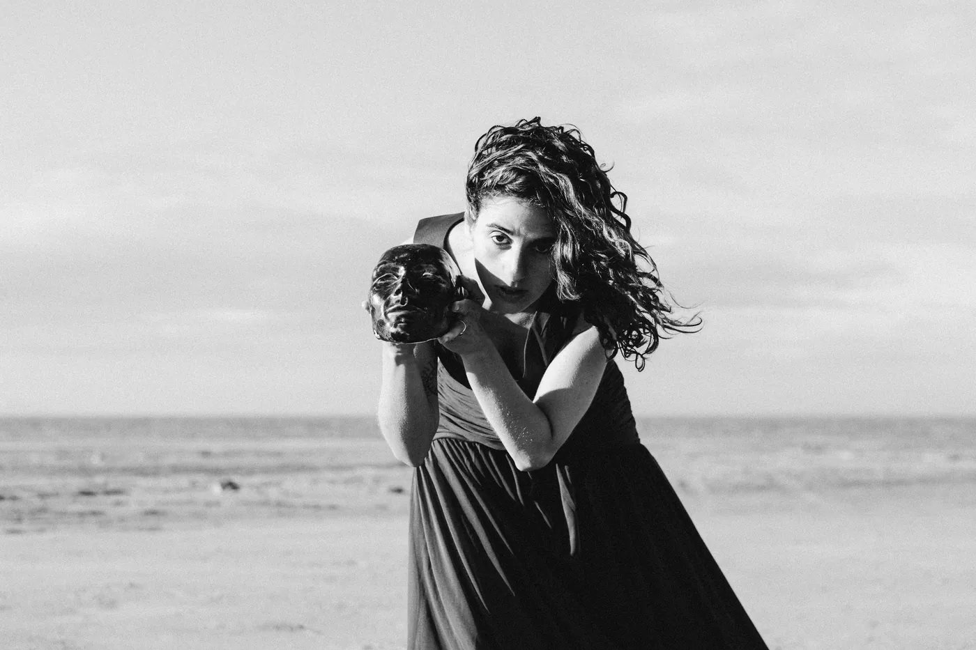 Vanessa Rosa by the sea, holding a ceramic head to her face, in black and white.