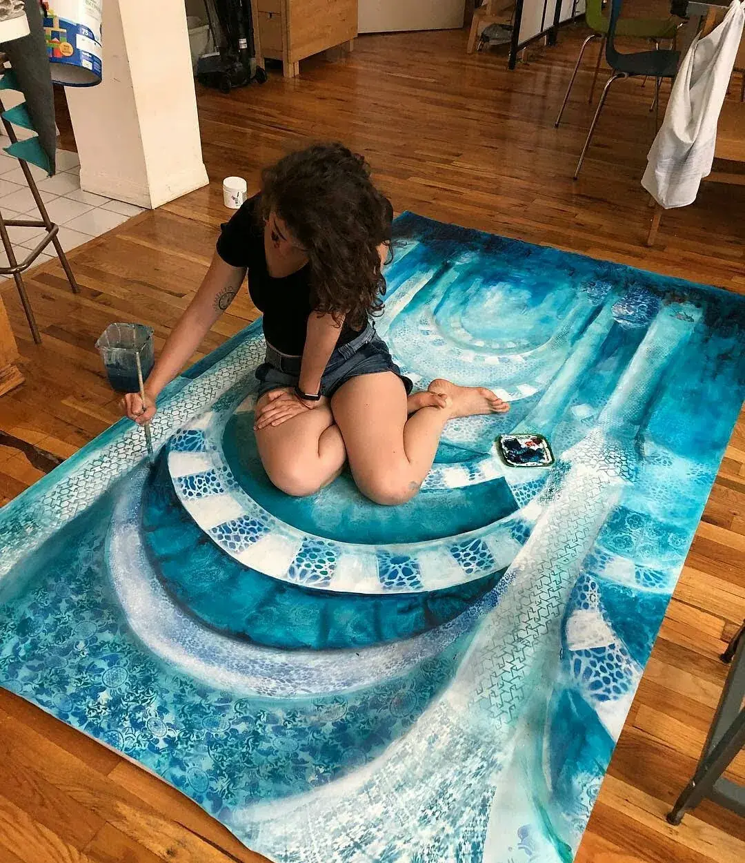 Vanessa Rosa kneeling on a large blue tile painting laid on a wooden floor.