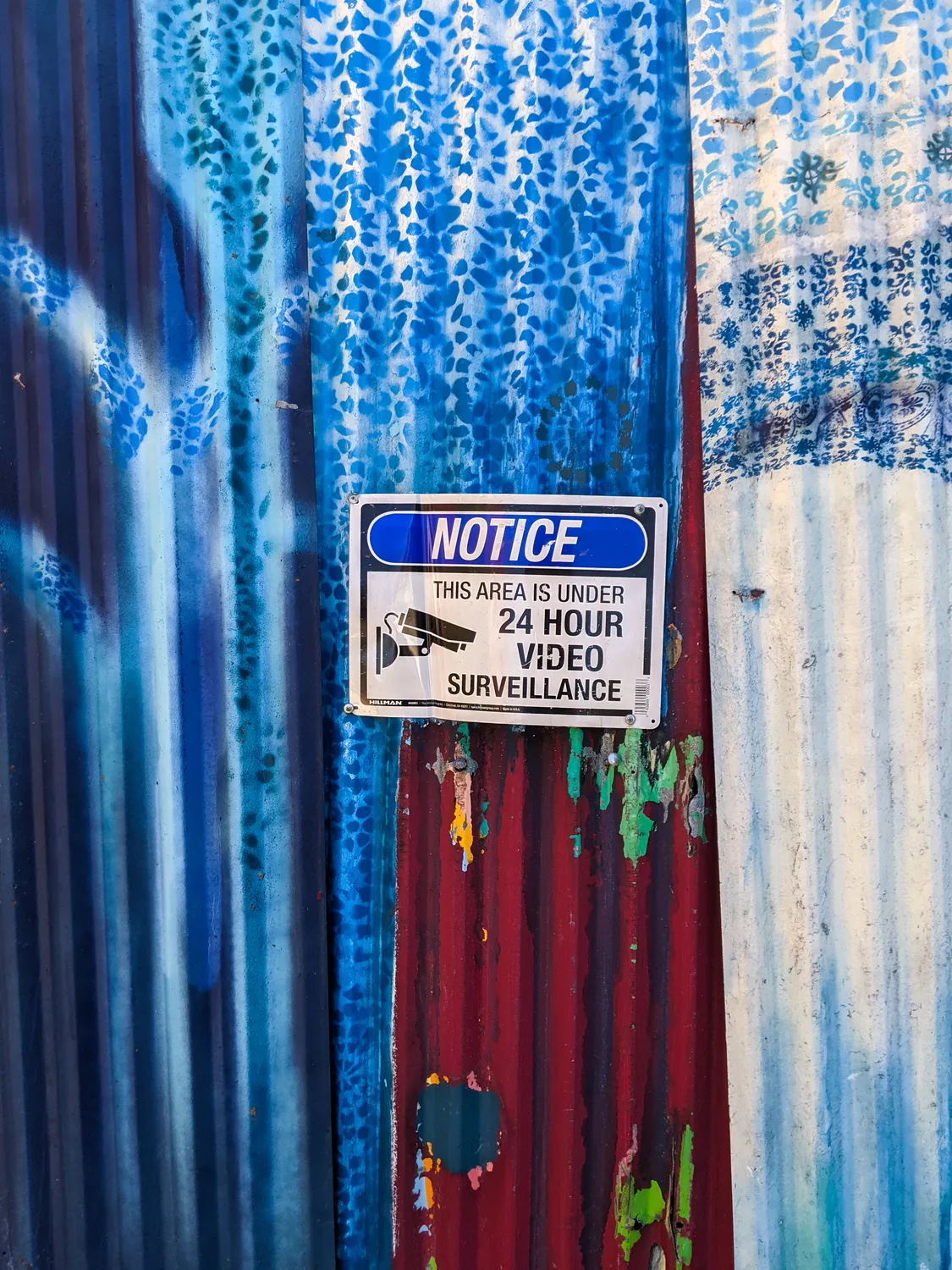 A surveillance notice bolted through the painting.
