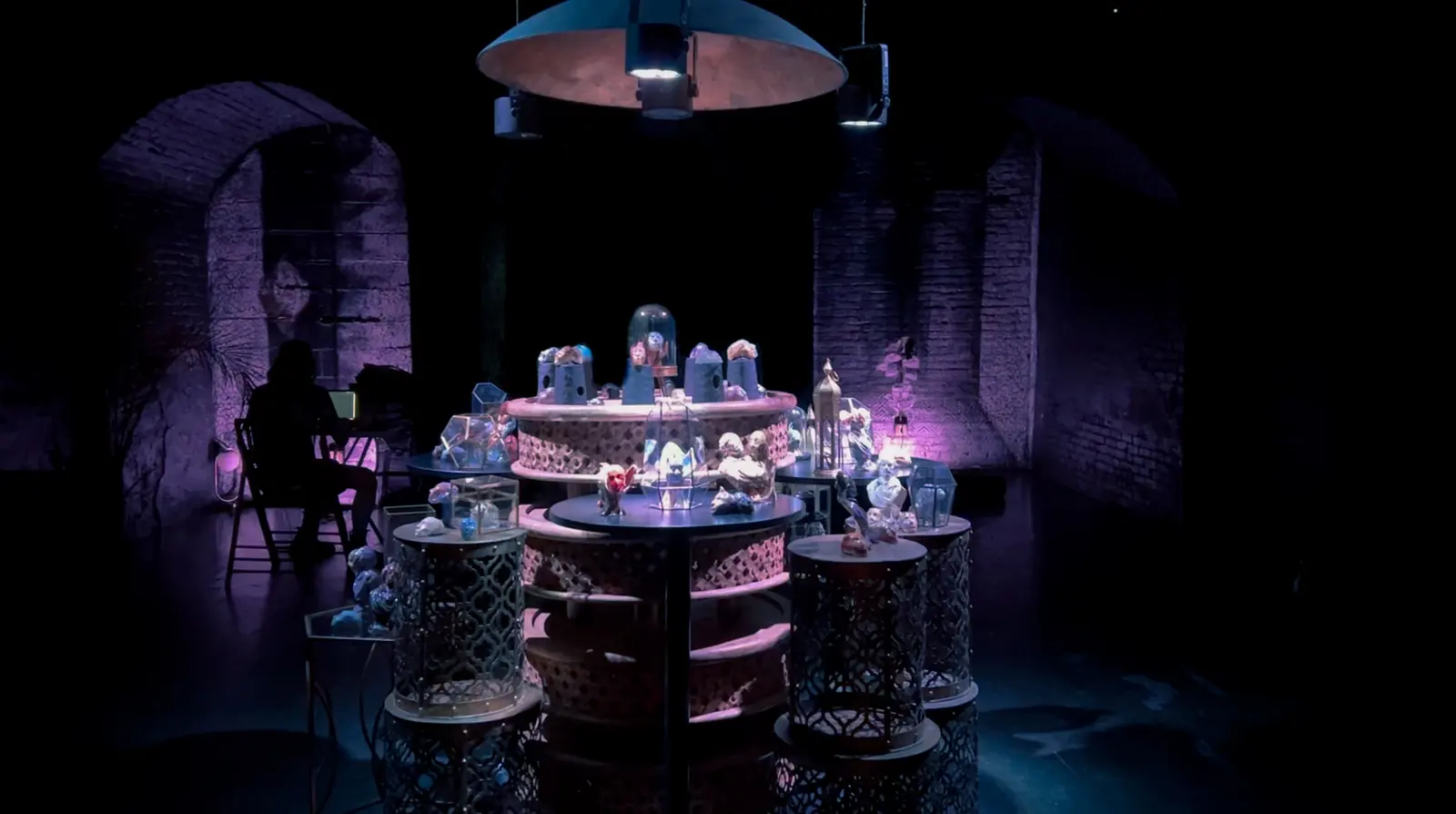 The pop-up seen across the room: round tables of lit glass cases under brick arches.