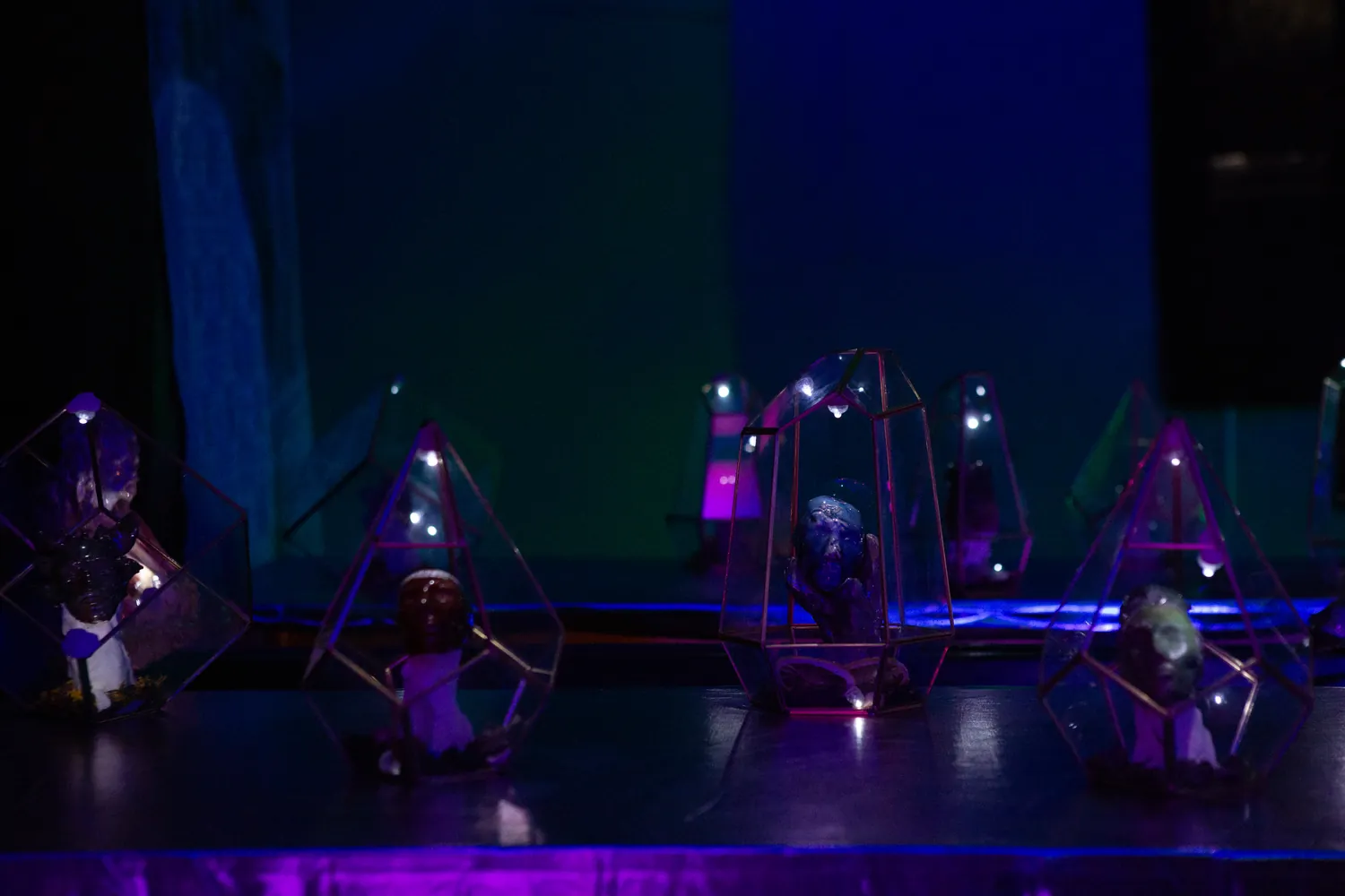 Glass cases holding ceramic heads, lit blue and violet in a dark room.