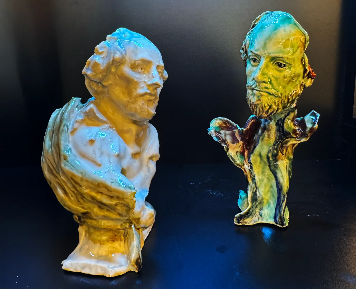 Two glazed ceramic busts of Shakespeare facing each other on a dark table.
