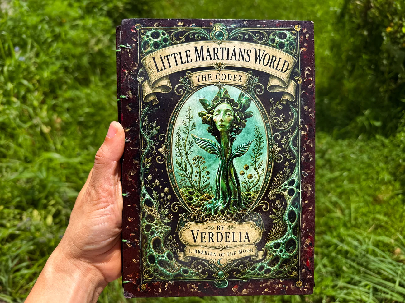 Little Martians World: The Codex, by Verdelia, Librarian of the Moon. The bound cover held up against grass.