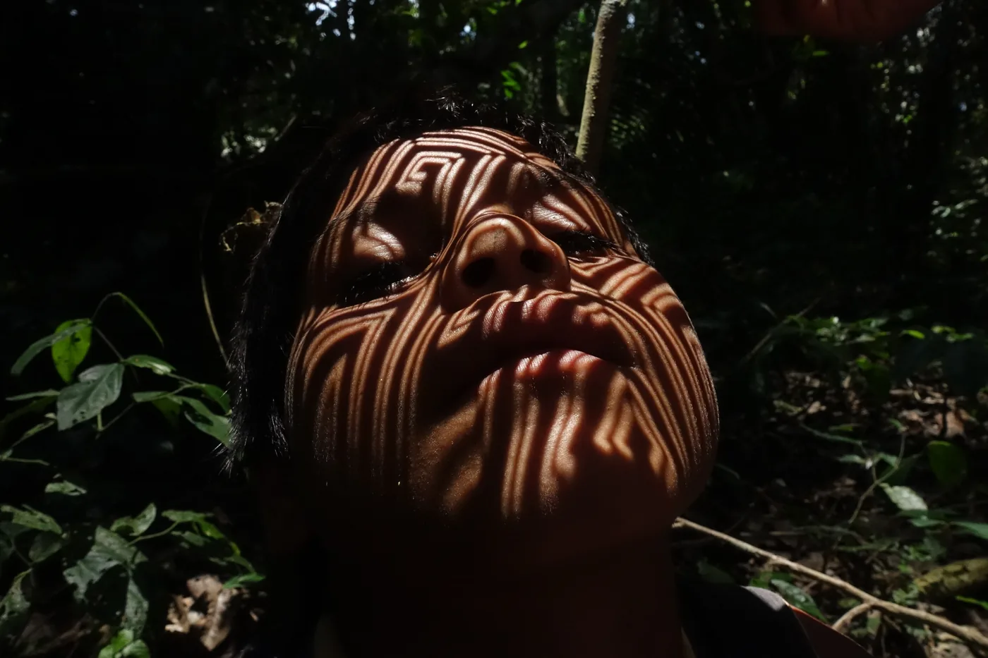 A Huni Kuin pattern cast onto a face by sunlight through a laser-cut stencil, in the forest on the upper Envira.