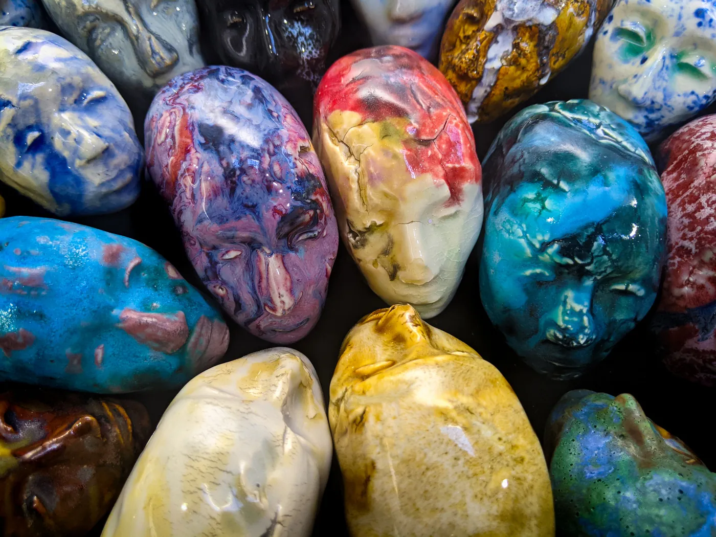 Two glazed ceramic Little Martian heads facing each other, one held in a hand, against black.