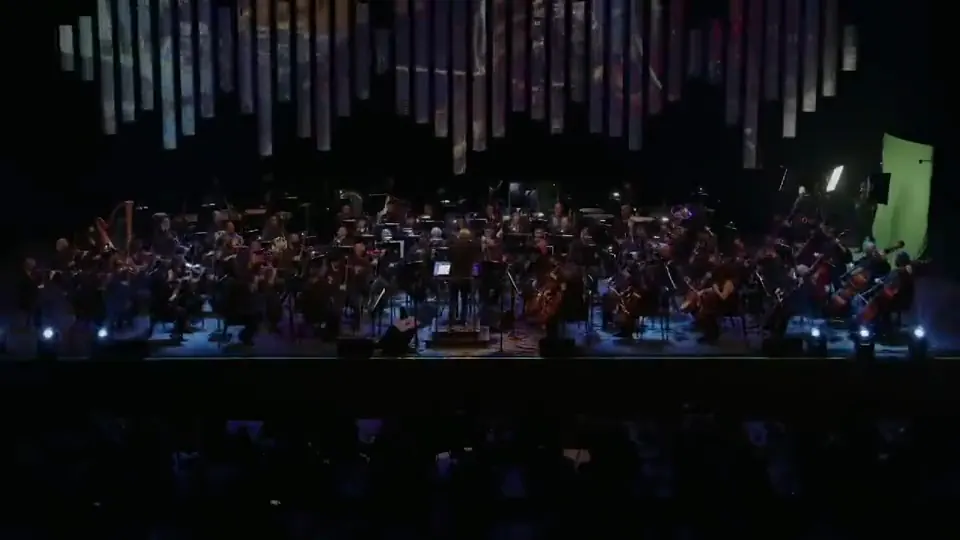 The orchestra on stage under a hanging installation of lit tubes.